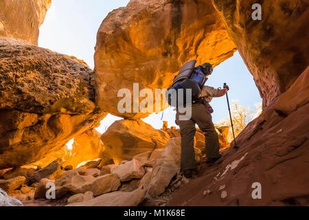 Hiker climbing a route through a sandstone fin within Salt Creek Canyon in The Needles District of Canyonlands National Park, Utah, USA Stock Photo