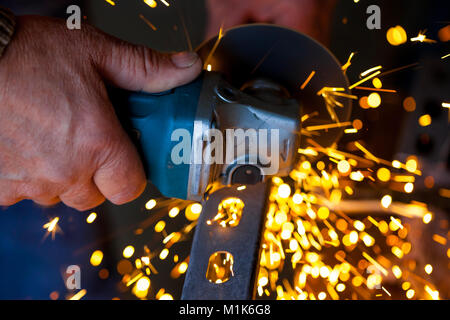 Man hand cuts metal bar usingelectric grinder with sparks flying around Stock Photo
