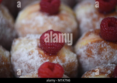 food image of some delicious fresh home made donuts or doughnuts coated in sugar with a jam filling and topped with a juicy red raspberry fruit Stock Photo