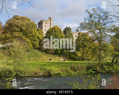 A glimpse of Haddon Hall through surrounding trees with the River Wye and lush water meadows in the foreground; near Bakewell, Derbyshire, UK Stock Photo