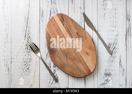 Oval cutting board with knife and fork on white wooden table background Stock Photo