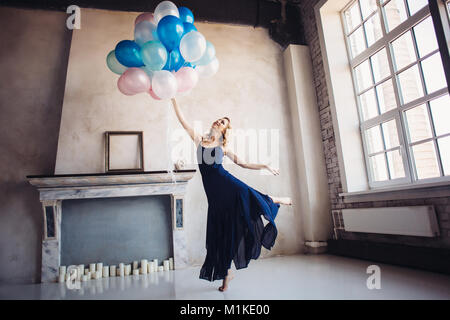 Blonde woman in blue dress dancing with blue and pink baloons, minimalist interior on background Stock Photo