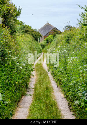Green lane with narrow winding track heading steeply down to a small house by the sea on the Dorset coast Stock Photo