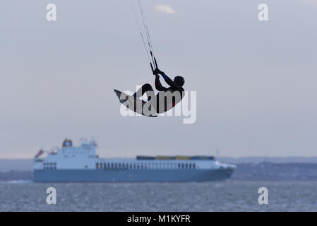 Kitesurfer on the Thames Estuary in the late afternoon, surfing with passing river traffic. Ship. Shipping. Kite surfer getting big air Stock Photo