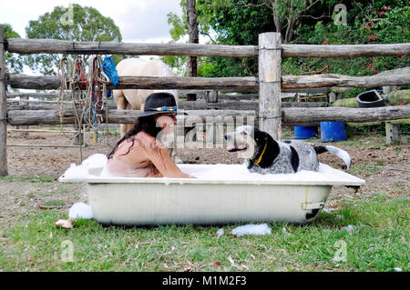 COWGIRL AND DOG  SITTING IN BATH WITH WET DRESS ON Stock Photo