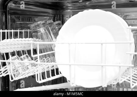 upper basket with freshly washed saucers and some glasses inside the dishwasher Stock Photo