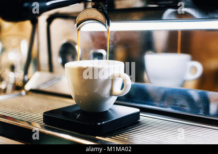 Professional espresso machine pouring fresh coffee into white ceramic cup with reflection on background Stock Photo
