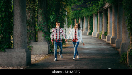 Walking cheerful young couple by the hand along the archway of Centennial Hall in Wroclaw, Poland overgrown with plants. Stock Photo