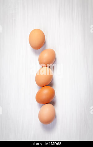 Five yellow eggs lie in a line on a white wooden table Stock Photo