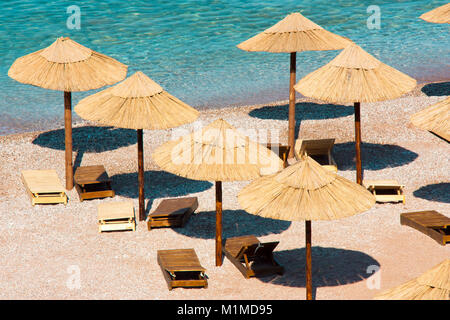 Perfect summer vacation destination : Straw sunshades and sunbeds on the empty pebble beach  with sea  in the background , high angle view Stock Photo