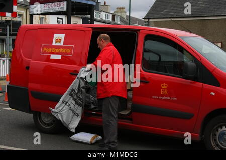 A RED PEUGEOT ROYAL MAIL DELIVERY VAN IN WELSH AND ENGLISH BILINGUAL LIVERY WITH POSTMAN EMPTYING MAIL INTO A SACK Stock Photo