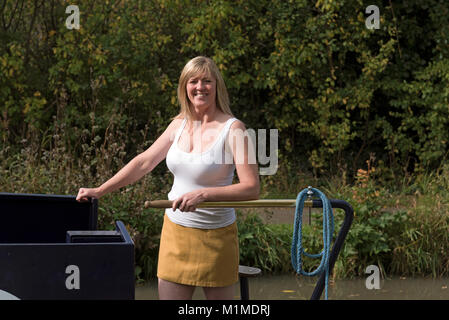 Woman using the tiller to steer a narrowboat along an English canal Stock Photo