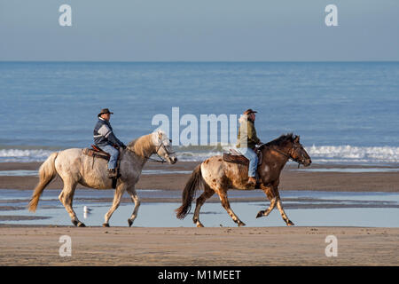 Elderly couple riding horseback on sandy beach along the North Sea coast on a cold day in winter Stock Photo