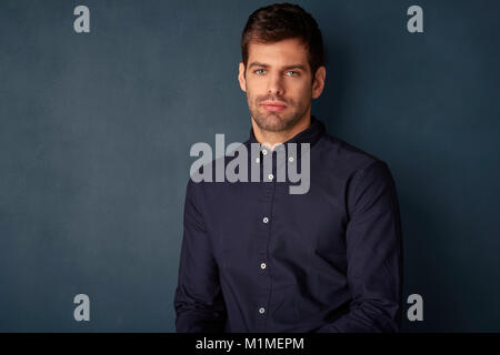 Close-up portrait of a confident young man wearing shirt and looking at camera while standing at dark background. Stock Photo