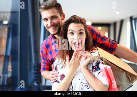 sale, consumerism and people concept - happy young couple with shopping bags walking in mall. Stock Photo