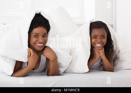 Smiling Mother And Daughter Lying On Bed Under The Blanket Stock Photo
