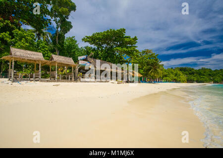 A row of structures with palm leaves thatched roofs on the almost empty beautiful beach in Siam Bay on Racha Island, Phuket, Thailand. Stock Photo