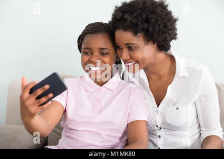 Smiling Mother And Daughter Taking Selfie On Smart Phone At Home Stock Photo