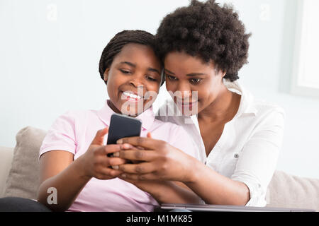 Mother And Daughter Sitting On Couch Looking At Smart Phone Stock Photo