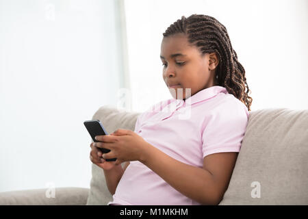 Close-up Of An African Girl Sitting On Couch Using Smart Phone Stock Photo