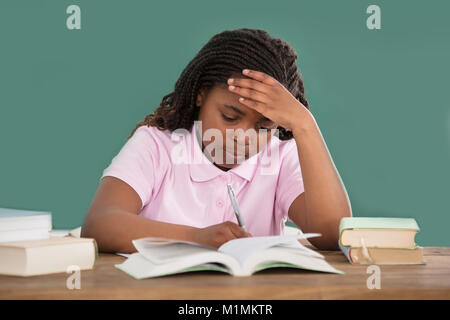 Portrait Of An African Girl Doing Studies In Classroom Against The Green Chalkboard Stock Photo