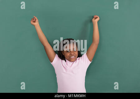 Happy African Girl Raising Her Hand Standing In Front Of Green Chalkboard Stock Photo