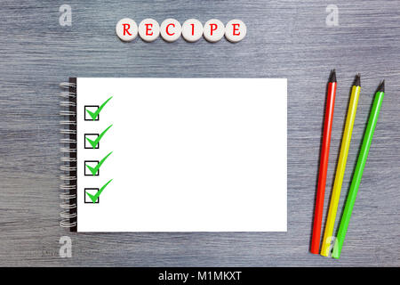 On the table is a white notebook with three pencils. Notepad with pencils and tablets with the inscription recipe Stock Photo