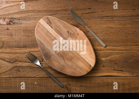 Oval cutting board with knife and fork on brown wooden table background Stock Photo