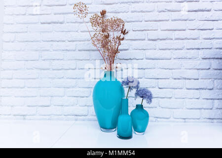 Wildflowers in turquoise vases standing on a white table against a white kerp wall. Wildflowers in a vase. Stock Photo