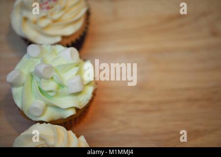 delicious cup cake with a light green swirl butter cream top and white marshmallows on a wood kitchen board Stock Photo