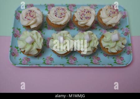 beautiful mini cupcakes in pastel colors laid on a small floral pattern tray with pink background Stock Photo