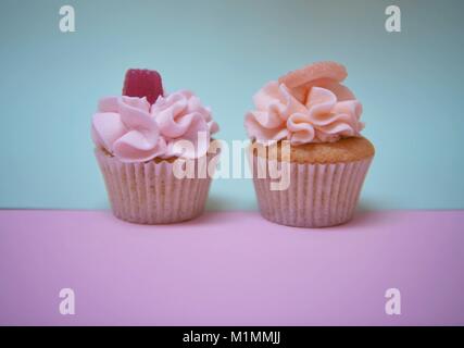 delicious handmade cupcakes with swirl iced frosting on top with a split tone pastel color background in pink and blue Stock Photo