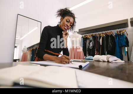 Fashion entrepreneur making a drawing at her desk. Female fashion designer sketching a design sitting in her cloth store.