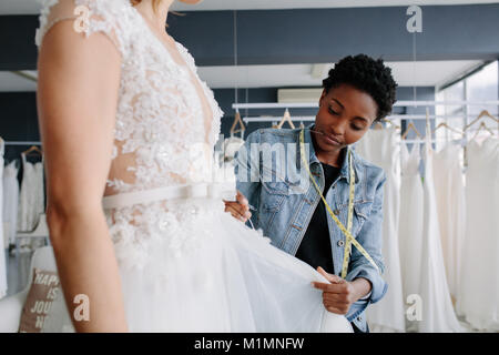 Professional wedding dress designer fitting bridal gown to woman in her store. Woman making adjustments to bridal gown in her boutique. Stock Photo