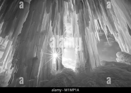 A sun burst shines around an ice column curtain on Grand Island near Munising Michigan in winter Stock Photo