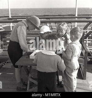 1950s, historical, on the ocean aboard a Union-Castle steamship headed for a new life in South Africa, a group of young children play together with small construciton plastic toys on a small table outside on the ship's deck. Stock Photo