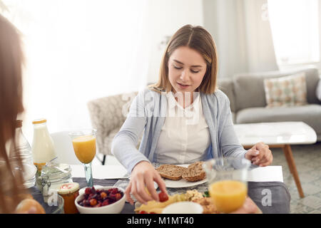Pretty young teenage woman smile sitting at a table with her best friend enjoying breakfast and turning and taking a fresh tomato Stock Photo