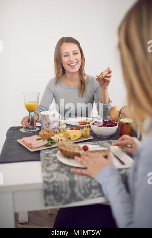 Pretty young teenage woman with a vivacious smile sitting at a table with her best friend enjoying breakfast and turning to smile at the camera Stock Photo