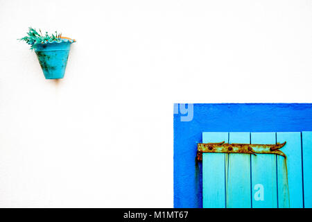 White stone wall with turquoise blue flower pot and portion of turquoise door with rusted hinge Stock Photo