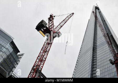 cranes working on a construction site next to or alongside the shard iconic office building and modern architecture in the centre of the capital city. Stock Photo