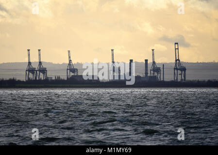 London Thamesport dock cranes on the River Medway across the Thames Estuary at dusk. Isle of Grain, Kent. View from Southend, Essex Stock Photo