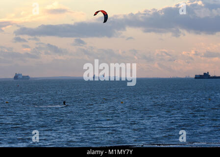 Kite surfer surfing in the Thames Estuary near Southend on Sea, Essex, UK, with cargo ships in the shipping lanes Stock Photo