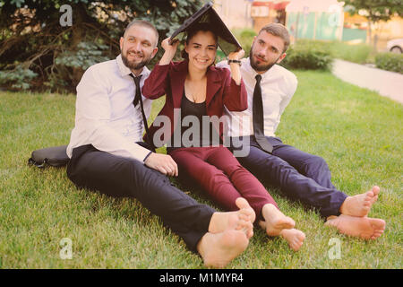 friends in business clothes and barefoot sitting on grass holding laptop in hands Stock Photo