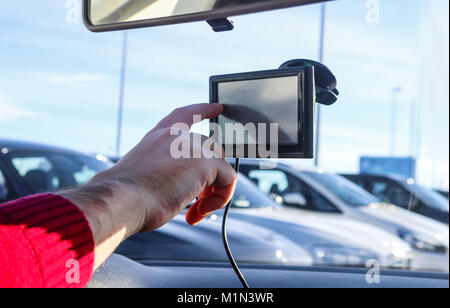 Man's hand inputting information into GPS in car with parked cars in the background Stock Photo