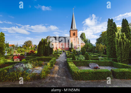 Old city cemetary and catholic church in Dragor, Denmark - September, 21th, 2015. Gravestones, greenery and cloud sky at the early morning in fishman  Stock Photo