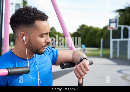 Young man at outdoor gym checking fitness app on smartwatch Stock Photo
