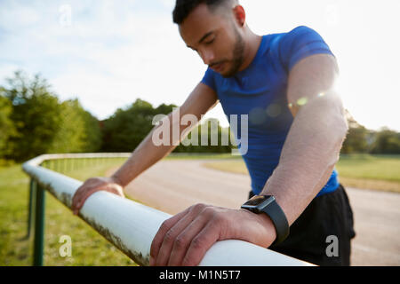 Male athlete leaning on fence at running track, close up Stock Photo