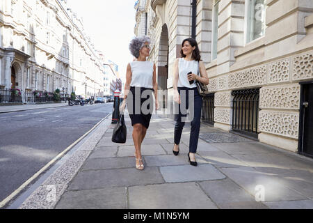 Two female colleagues walking in the street talking Stock Photo