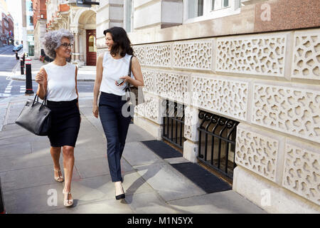Two women walking in the street talking, full length Stock Photo