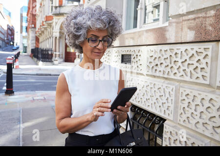 Middle aged woman using smartphone in city street Stock Photo